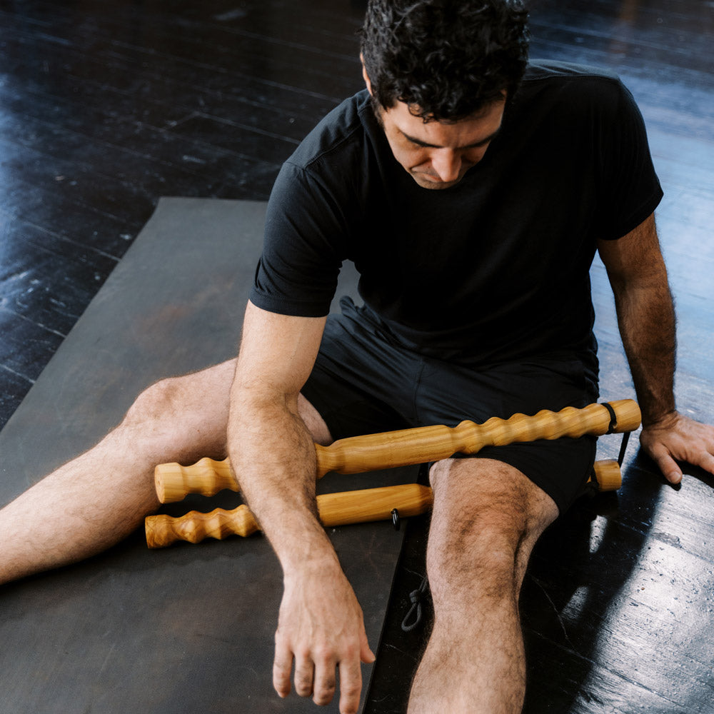 Man using a wooden roller on his leg to massage his muscles.