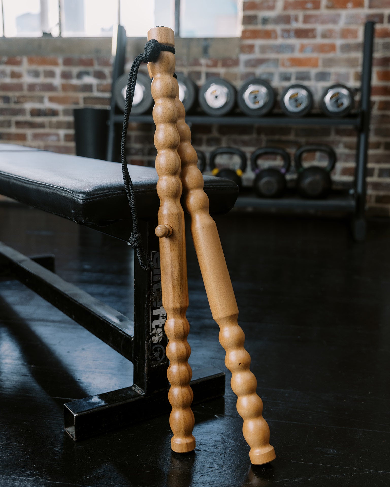 Body Lever wooden massage tool sticks propped up against a workout bench with a brick wall background