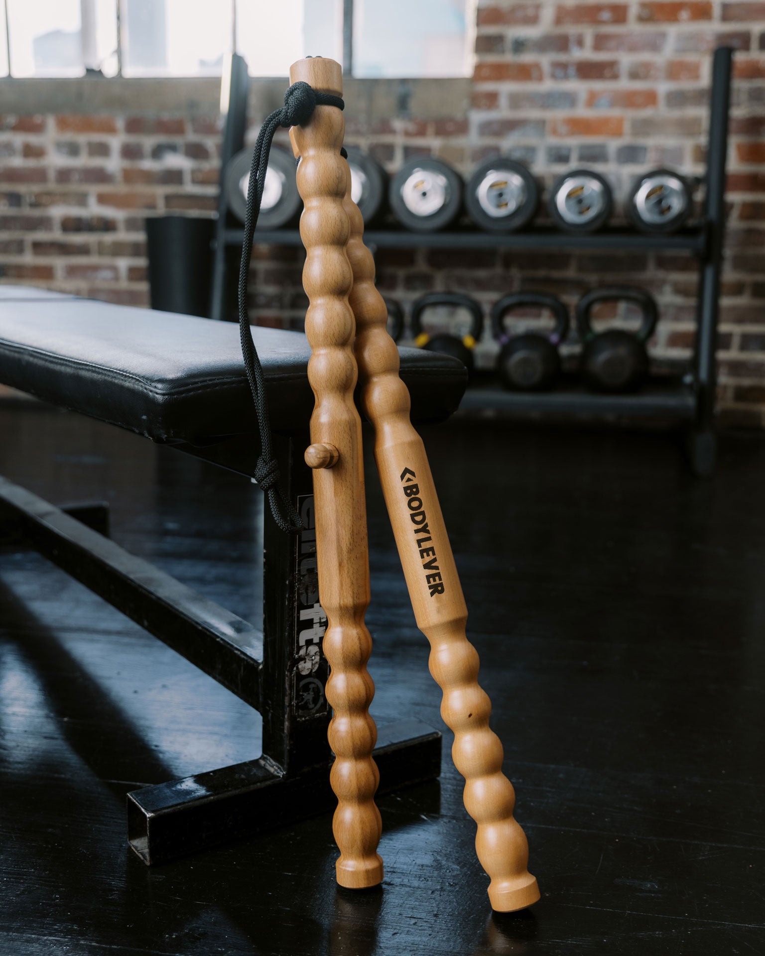 BodyLever wooden massage tool sticks propped up against a workout bench with a brick wall background