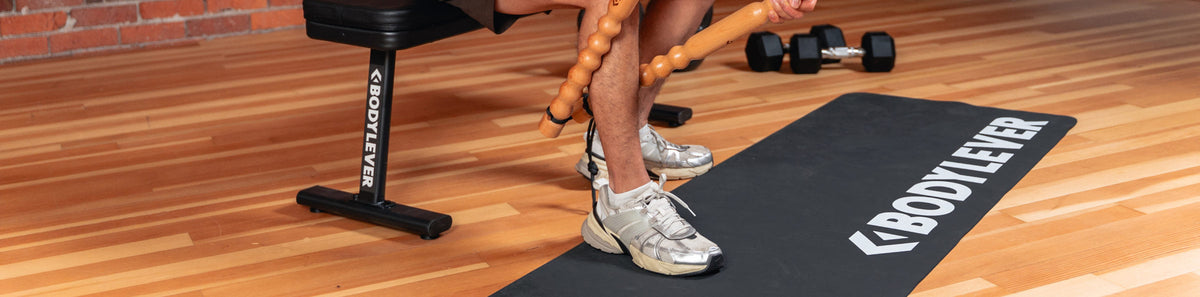 Man's legs in a gym with BodyLever massage tool and yoga mat.
