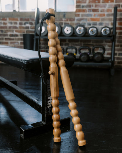 Body Lever wooden massage tool sticks propped up against a workout bench with a brick wall background