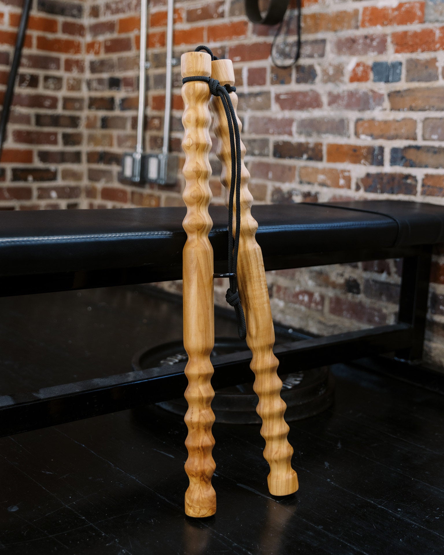 Wooden massage bar tool leaning on a black workout bench with a brick wall background